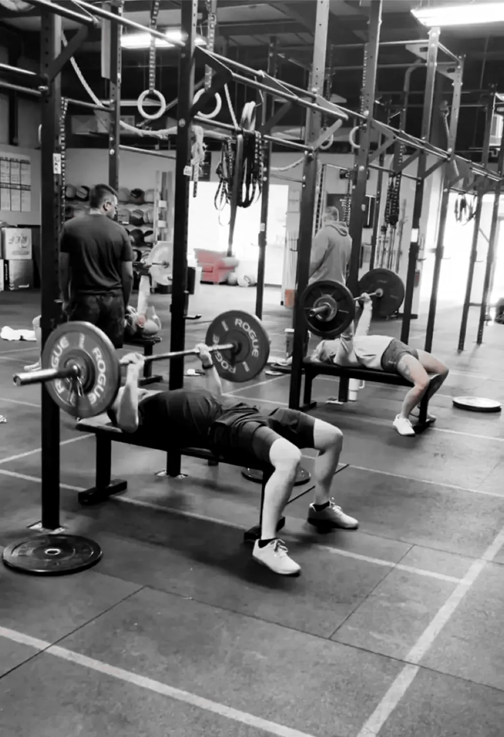 A member working a bench press with a coach nearby